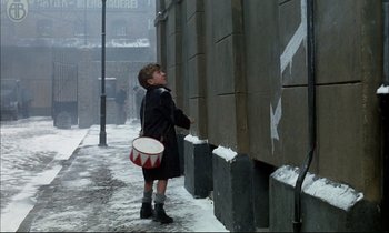 Movie still from “The Tin Drum” (1979), directed by Volker Schlöndorff – A young boy holding a drum on a snowy day; Wide shot, Over the shoulder angle