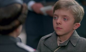 Movie still from “The Tin Drum” (1979), directed by Volker Schlöndorff – A young boy in a gray coat looking at a woman in a gray coat; Close Up shot, Over the shoulder angle