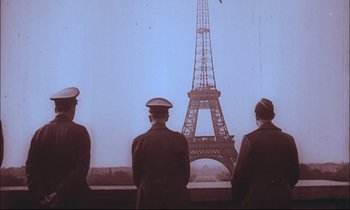 Movie still from “The Tin Drum” (1979), directed by Volker Schlöndorff – A group of men standing next to each other in front of the eiffel tower; Wide shot, Low angle