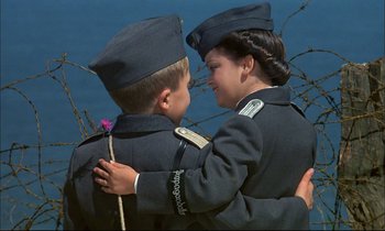Movie still from “The Tin Drum” (1979), directed by Volker Schlöndorff – A young boy and a woman dressed in military uniforms; Close Up shot, High angle
