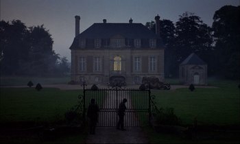 Movie still from “The Tin Drum” (1979), directed by Volker Schlöndorff – Two people standing in front of a large house; Extreme Wide shot, Low angle
