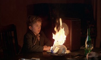 Movie still from “The Tin Drum” (1979), directed by Volker Schlöndorff – A young boy sitting in front of a fire; Medium shot, High angle