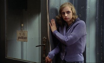 Movie still from “The Tin Drum” (1979), directed by Volker Schlöndorff – A woman leaning against a wall in front of a door; Medium shot, Over the shoulder angle
