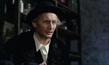 Movie still from “The Tin Drum” (1979), directed by Volker Schlöndorff – A man wearing a black hat and a white shirt; Close Up shot, Over the shoulder angle