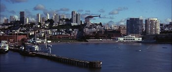 Movie still from “The Towering Inferno” (1974), directed by John Guillermin – A helicopter flying over a large body of water near a city; Extreme Wide shot, High angle