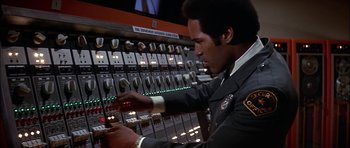 Movie still from “The Towering Inferno” (1974), directed by John Guillermin – A man in a police uniform working on an electrical panel; Close Up shot, Low angle