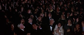 Movie still from “The Towering Inferno” (1974), directed by John Guillermin – A group of people in the audience at a movie; Wide shot, Low angle