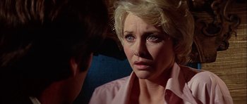 Movie still from “The Towering Inferno” (1974), directed by John Guillermin – An older blonde woman looking sad while talking to a younger man; Close Up shot, Over the shoulder angle
