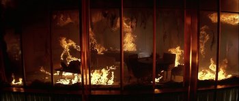Movie still from “The Towering Inferno” (1974), directed by John Guillermin – A fire is burning in a living room with chairs; Extreme Wide shot, High angle