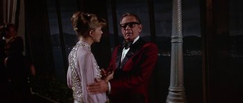 Movie still from “The Towering Inferno” (1974), directed by John Guillermin – An older man in a red jacket talking to a woman in a pink dress; Medium shot, Over the shoulder angle
