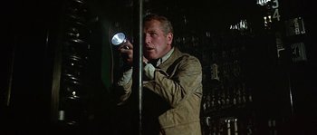 Movie still from “The Towering Inferno” (1974), directed by John Guillermin – A man holding a flashlight while standing next to a wall; Medium shot, Low angle