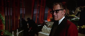 Movie still from “The Towering Inferno” (1974), directed by John Guillermin – A man in a suit and glasses is standing in front of a fireplace; Close Up shot, Low angle