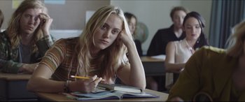 Movie still from “The Tribes of Palos Verdes” (2017), directed by Brendan Malloy – A woman sitting at a table with a book and pencil; Medium shot, Low angle