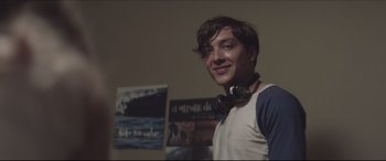 Movie still from “The Tribes of Palos Verdes” (2017), directed by Brendan Malloy – A young man with headphones around his neck smiles; Close Up shot, Over the shoulder angle