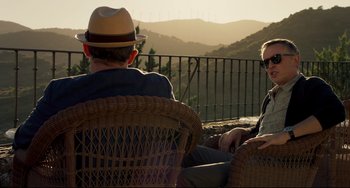 Movie still from “The Trip to Spain” (2017), directed by Michael Winterbottom – Two men sitting in a chair looking out at the mountains; Medium shot, Over the shoulder angle