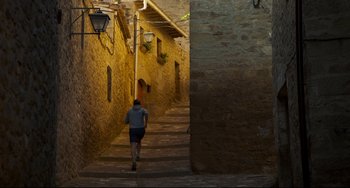 Movie still from “The Trip to Spain” (2017), directed by Michael Winterbottom – A man running down the side of a street; Extreme Wide shot, Low angle