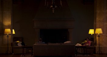 Movie still from “The Trip to Spain” (2017), directed by Michael Winterbottom – A man sitting in front of a fire place; Wide shot, High angle