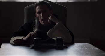Movie still from “The Trip to Spain” (2017), directed by Michael Winterbottom – A man sitting at a table with a knife in his hand; Medium shot, High angle