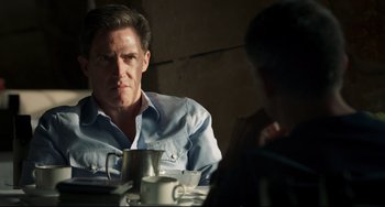 Movie still from “The Trip to Spain” (2017), directed by Michael Winterbottom – A man sitting at a table with a cup in front of him; Medium shot, Over the shoulder angle