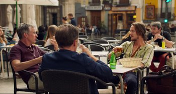 Movie still from “The Trip to Spain” (2017), directed by Michael Winterbottom – A group of people sitting at a table drinking beer; Medium shot, Over the shoulder angle
