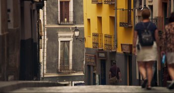 Movie still from “The Trip to Spain” (2017), directed by Michael Winterbottom – A man walking down a street near a tall building; Extreme Wide shot, Low angle