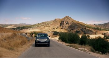 Movie still from “The Trip to Spain” (2017), directed by Michael Winterbottom – A car driving down a road near a hill; Extreme Wide shot, High angle