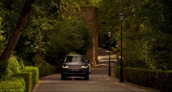 Movie still from “The Trip to Spain” (2017), directed by Michael Winterbottom – A car driving down a street next to trees and bushes; Extreme Wide shot, Low angle