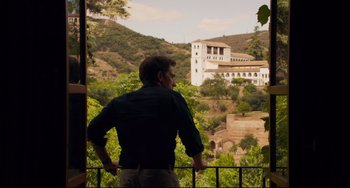 Movie still from “The Trip to Spain” (2017), directed by Michael Winterbottom – A man standing on a balcony looking out at a building; Wide shot, Low angle