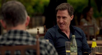 Movie still from “The Trip to Spain” (2017), directed by Michael Winterbottom – A man sitting at a table with a bottle of wine; Close Up shot, Over the shoulder angle