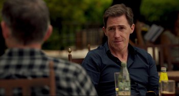 Movie still from “The Trip to Spain” (2017), directed by Michael Winterbottom – A man sitting at a table in front of a bottle of wine; Close Up shot, Over the shoulder angle