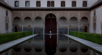 Movie still from “The Trip to Spain” (2017), directed by Michael Winterbottom – A man standing in front of a pool of water in front of a building; Extreme Wide shot, High angle