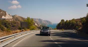 Movie still from “The Trip to Spain” (2017), directed by Michael Winterbottom – A car driving down a curvy road near the ocean; Extreme Wide shot, High angle