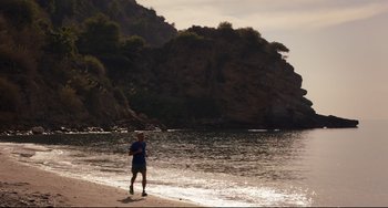 Movie still from “The Trip to Spain” (2017), directed by Michael Winterbottom – A man running on the beach near the water; Extreme Wide shot, High angle