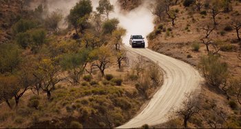 Movie still from “The Trip to Spain” (2017), directed by Michael Winterbottom – A truck driving down a dirt road in the middle of the desert; Extreme Wide shot, High angle