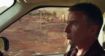 Movie still from “The Trip to Spain” (2017), directed by Michael Winterbottom – A man sitting in the passenger seat of a car looking out the window; Close Up shot, Over the shoulder angle