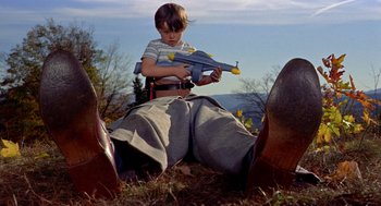 Movie still from “The Trouble with Harry” (1955), directed by Alfred Hitchcock – A young boy holding a toy gun next to a man's feet; Wide shot, Low angle