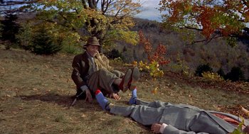 Movie still from “The Trouble with Harry” (1955), directed by Alfred Hitchcock – A man sitting on the ground next to a dead body; Wide shot, High angle