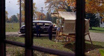 Movie still from “The Trouble with Harry” (1955), directed by Alfred Hitchcock – Two men standing in front of an easel and a car; Wide shot, High angle
