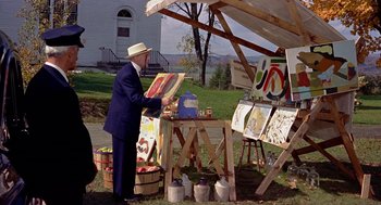 Movie still from “The Trouble with Harry” (1955), directed by Alfred Hitchcock – An older man in a blue suit painting a picture; Wide shot, High angle