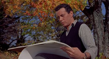 Movie still from “The Trouble with Harry” (1955), directed by Alfred Hitchcock – A man sitting down reading a magazine in front of a tree; Medium shot, Low angle