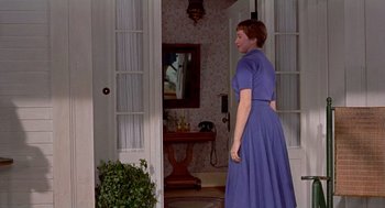 Movie still from “The Trouble with Harry” (1955), directed by Alfred Hitchcock – A woman in a blue dress standing in front of an open door; Medium shot, Over the shoulder angle