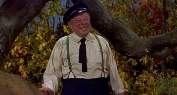 Movie still from “The Trouble with Harry” (1955), directed by Alfred Hitchcock – An older man wearing a hat and suspenders standing next to a tree; Medium shot, Low angle