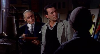 Movie still from “The Trouble with Harry” (1955), directed by Alfred Hitchcock – A man in a suit and tie standing next to another man in a suit and tie; Medium shot, Over the shoulder angle