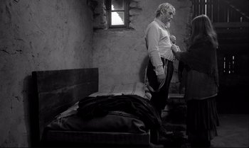 Movie still from “The Turin Horse” (2011), directed by Ágnes Hranitzky – A man standing next to a bed in a room; Medium shot, Over the shoulder angle