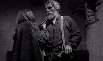 Movie still from “The Turin Horse” (2011), directed by Ágnes Hranitzky – An old man with a long gray beard is tying a woman's neck tie; Medium shot, Over the shoulder angle