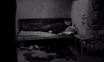 Movie still from “The Turin Horse” (2011), directed by Ágnes Hranitzky – A man laying on a bed in a room; Wide shot, Overhead angle