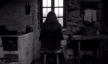 Movie still from “The Turin Horse” (2011), directed by Ágnes Hranitzky – A woman sitting in a chair looking out of a window; Wide shot, High angle