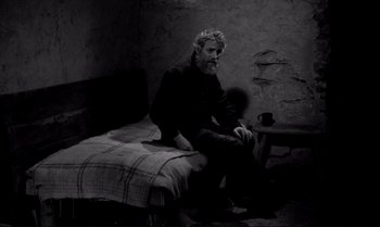 Movie still from “The Turin Horse” (2011), directed by Ágnes Hranitzky – A man sitting on top of a bed next to a coffee mug; Wide shot, High angle