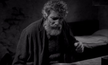 Movie still from “The Turin Horse” (2011), directed by Ágnes Hranitzky – An old man with a beard is sitting at a table; Medium shot, High angle