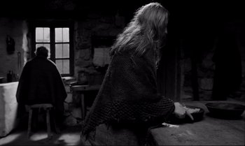 Movie still from “The Turin Horse” (2011), directed by Ágnes Hranitzky – A woman sitting in front of a stone wall; Medium shot, Over the shoulder angle